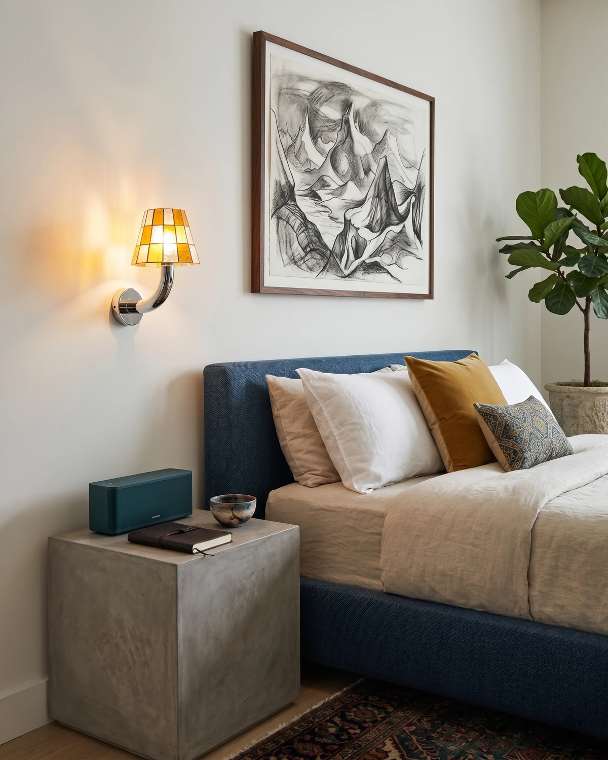 Stained glass wall sconce TESSERA No.01 in amber lit above a blue upholstered bed next to a concrete side table