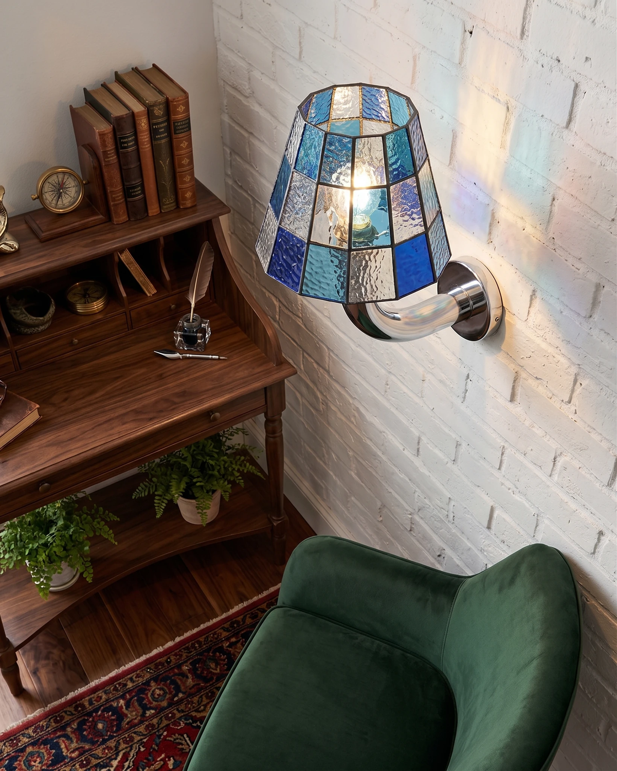 Stained glass wall sconce TESSERA No.01 in blue mosaic lit on a white brick wall above a walnut writing desk