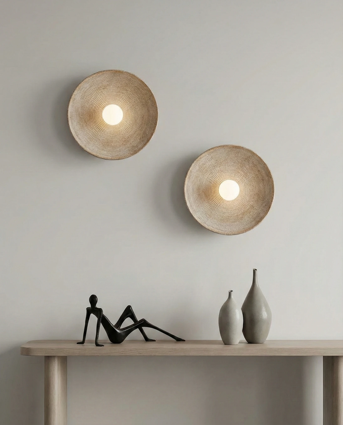 Stone-look wall sconce ECCO No.01, two cream units lit above a console table with vases and a figurine