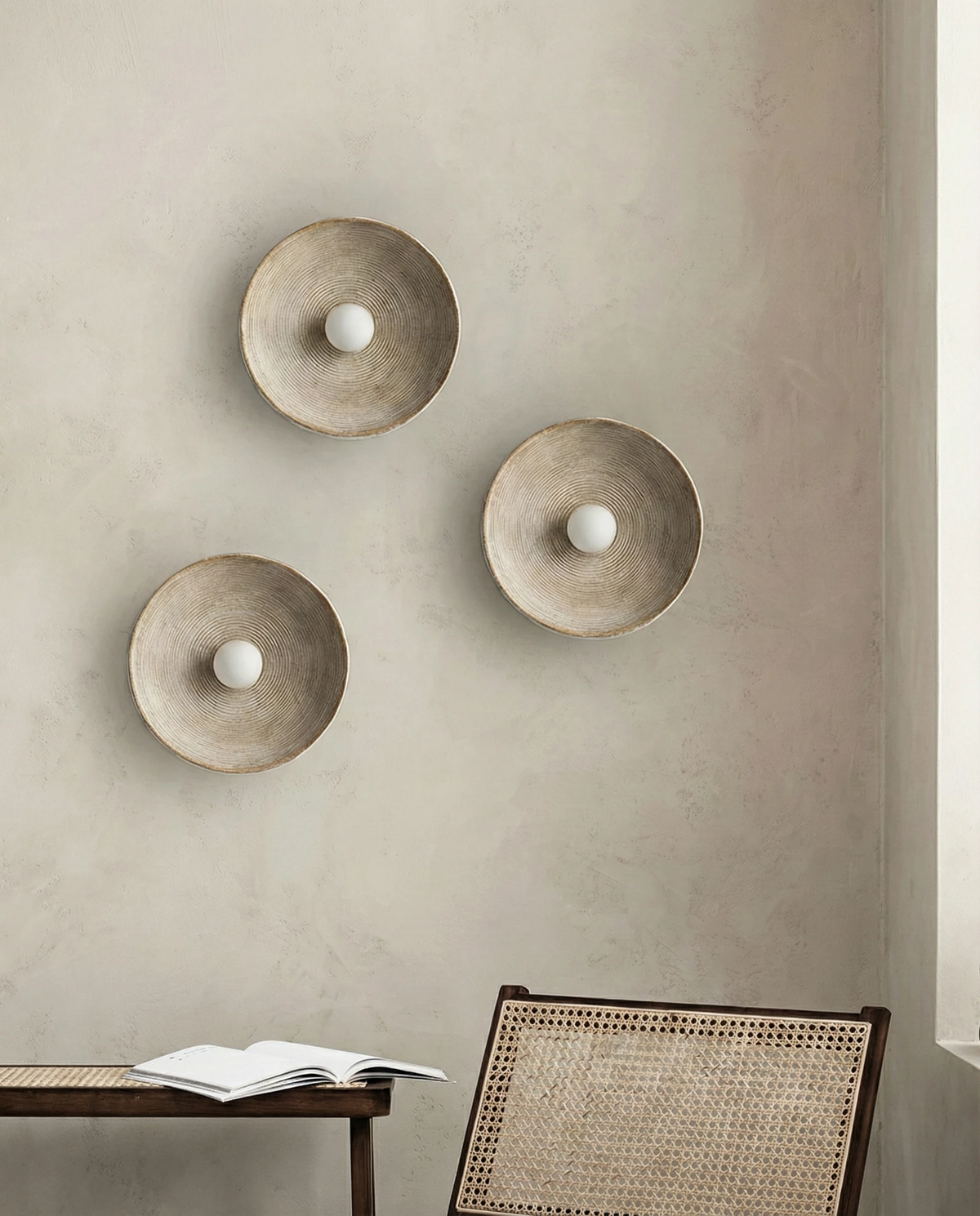 Stone-look wall sconce ECCO No.01, three cream units clustered on a wall above a wooden desk with a cane chair