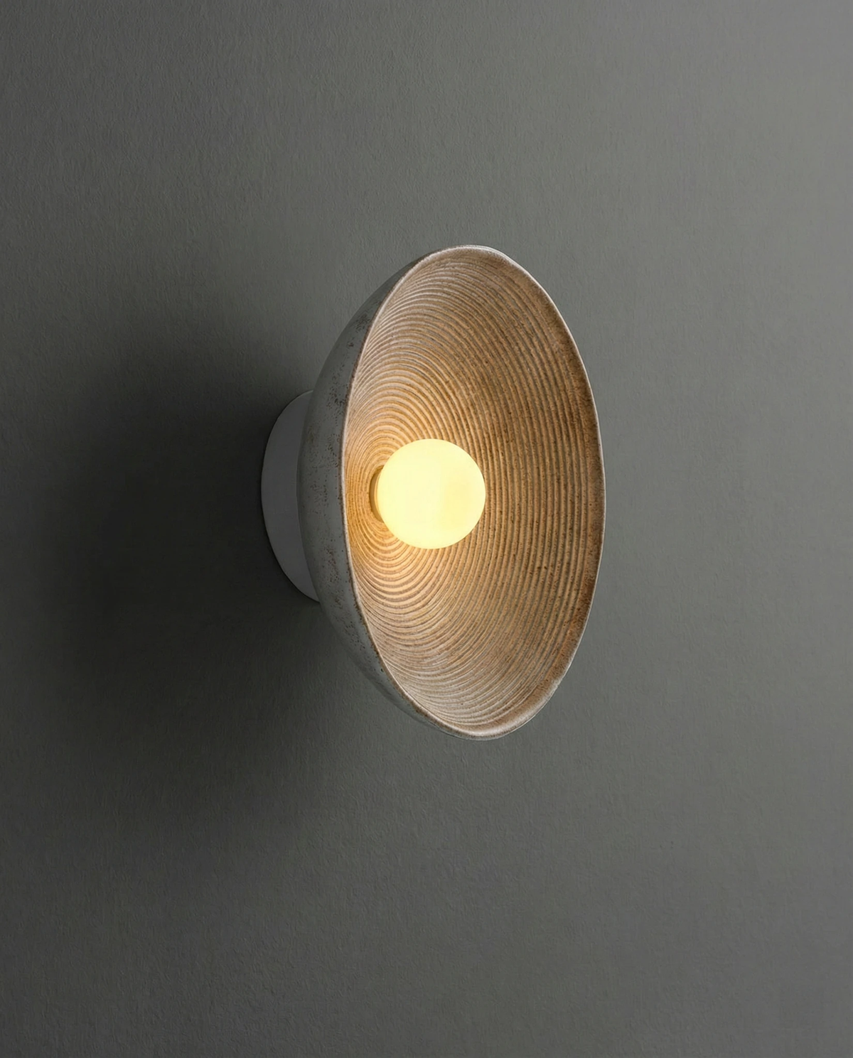 Stone-look wall sconce ECCO No.01 seen from the side on a dark gray wall, ridged bowl lit from the center