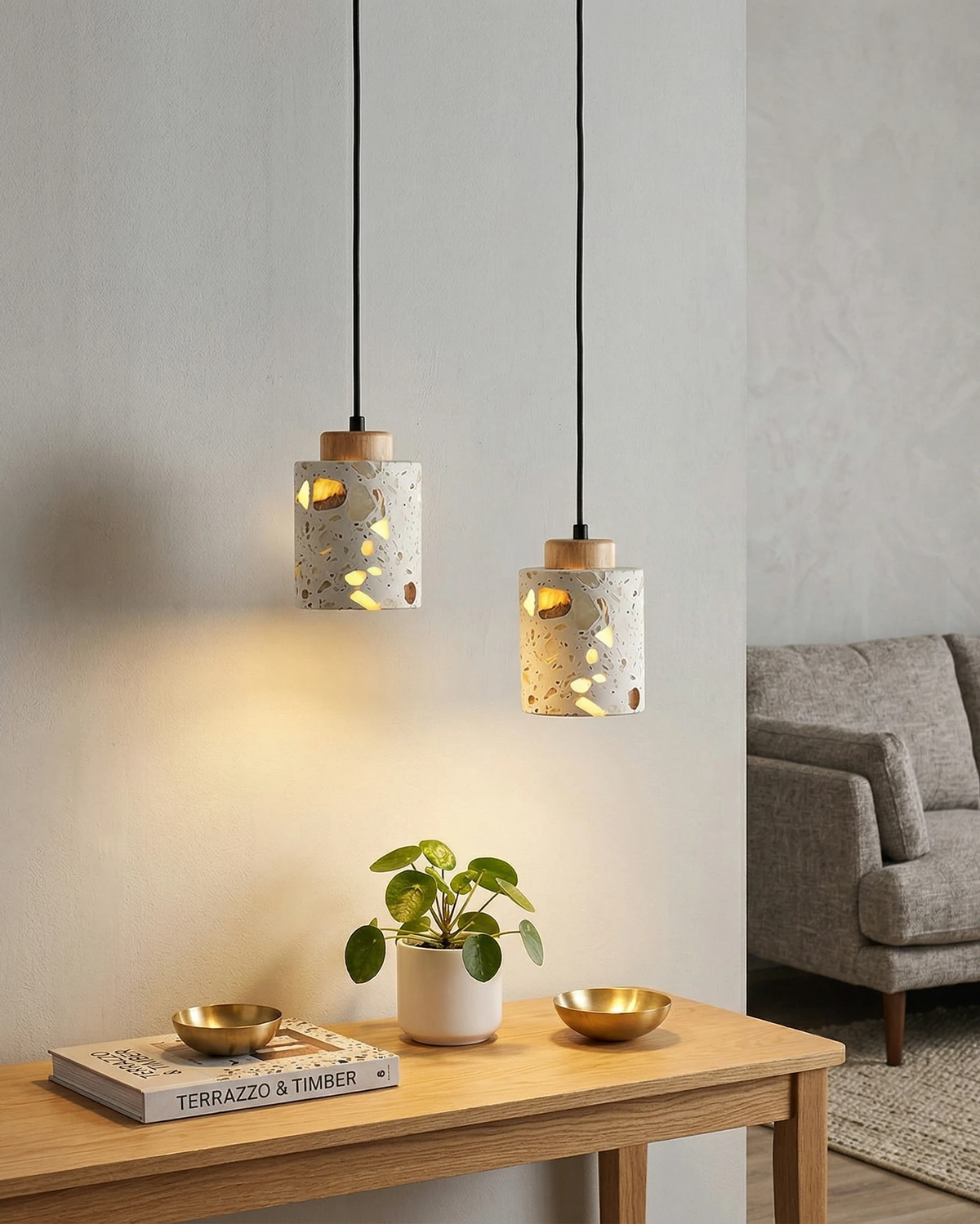 Two terrazzo pendant lights GROTTA No.01 cylinder with natural wood caps lit above an oak console with a plant