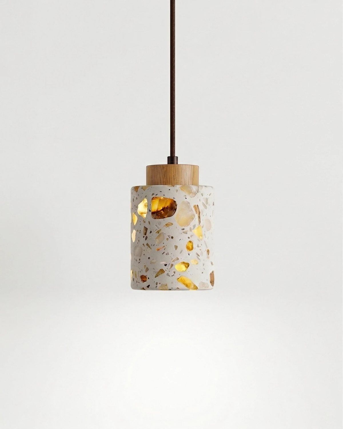 Terrazzo pendant light GROTTA No.01 cylinder with natural wood cap, switched on against a white background