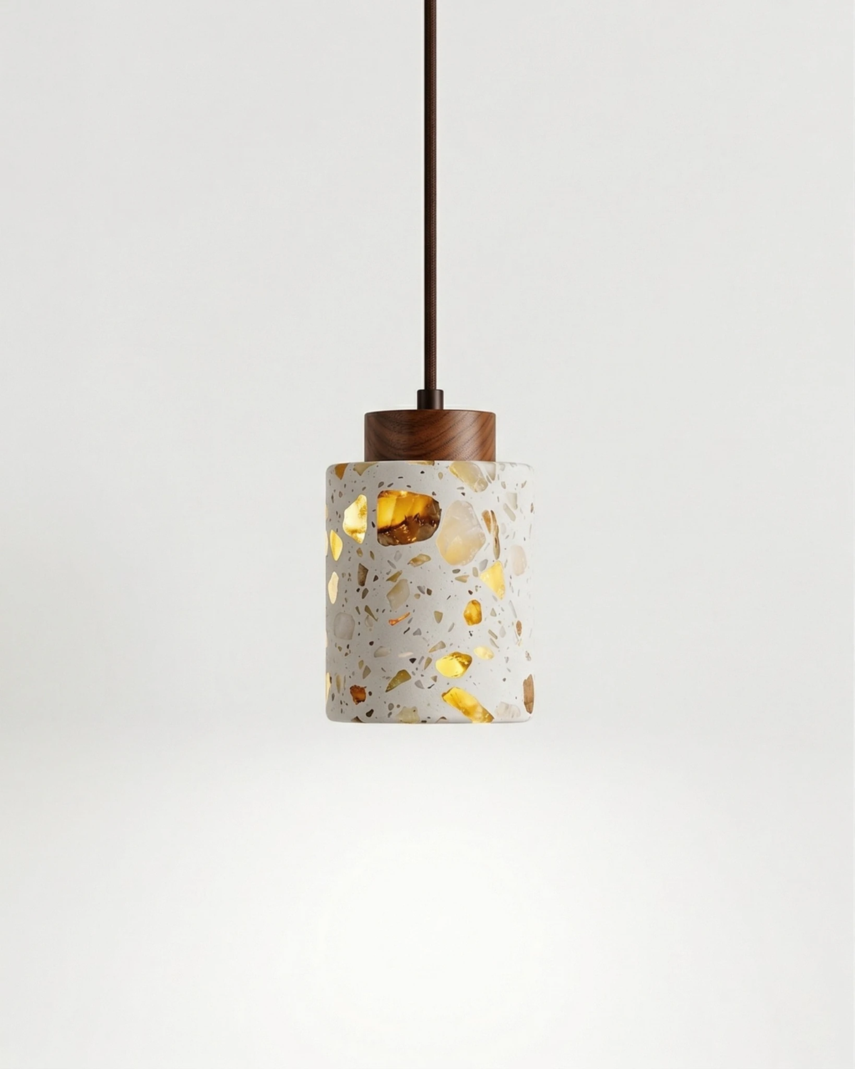 Terrazzo pendant light GROTTA No.01 cylinder with walnut cap, switched on and glowing through the gold flecks