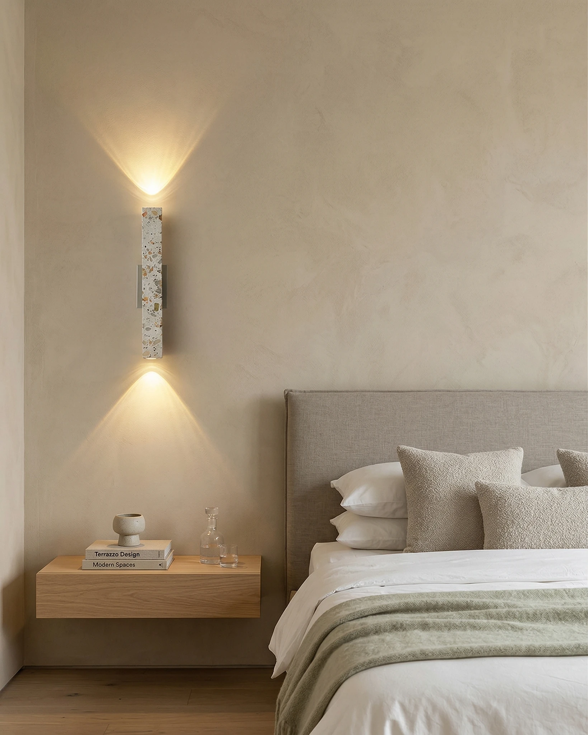 Terrazzo wall sconce PARMA No.01 lit up and down beside a gray upholstered headboard and floating oak nightstand