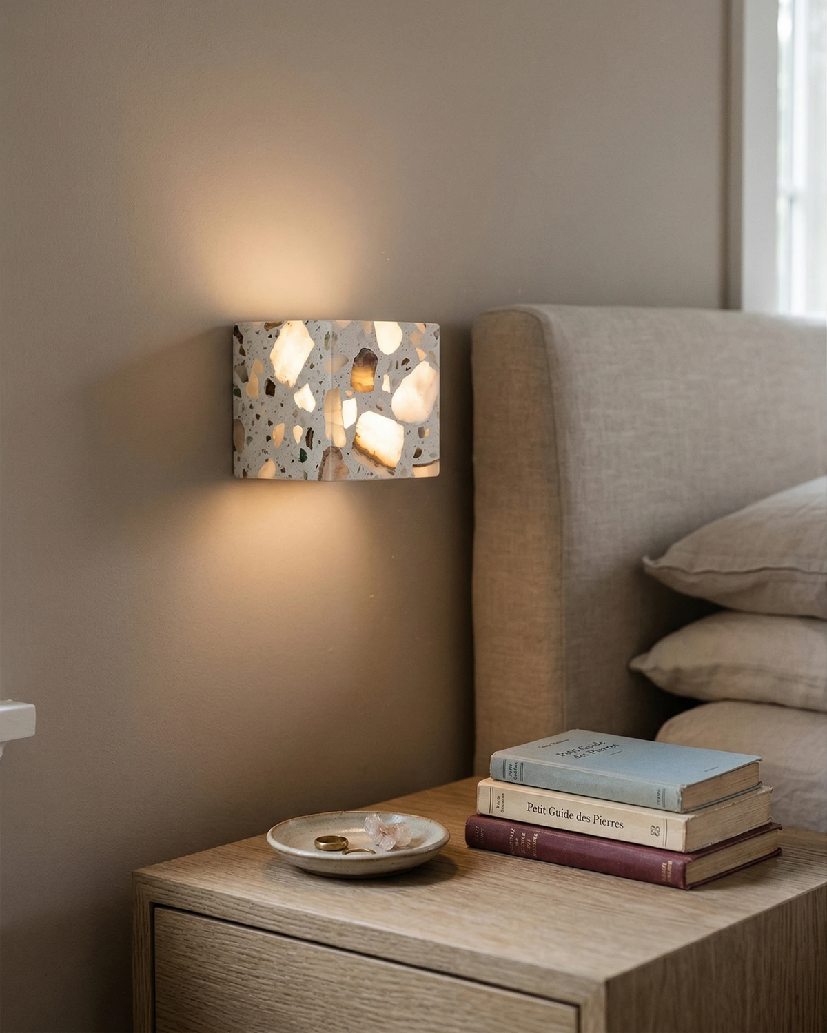 Terrazzo wall sconce INCA No.01 rectangle lit beside a bed with an upholstered headboard and a nightstand with books