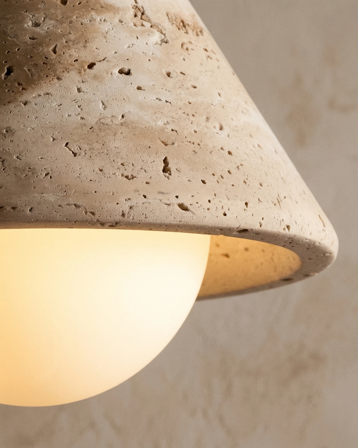 Close-up of the pitted travertine cone and glowing opal globe of the travertine flush mount ceiling light CIPRO No.01