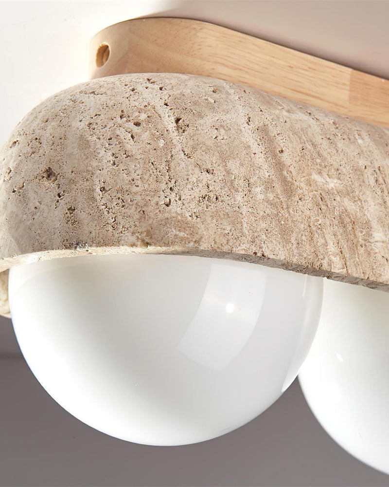Close-up of the pitted stone bar, light wood cap and opal globe of the PIETRA No.03 travertine flush mount ceiling light
