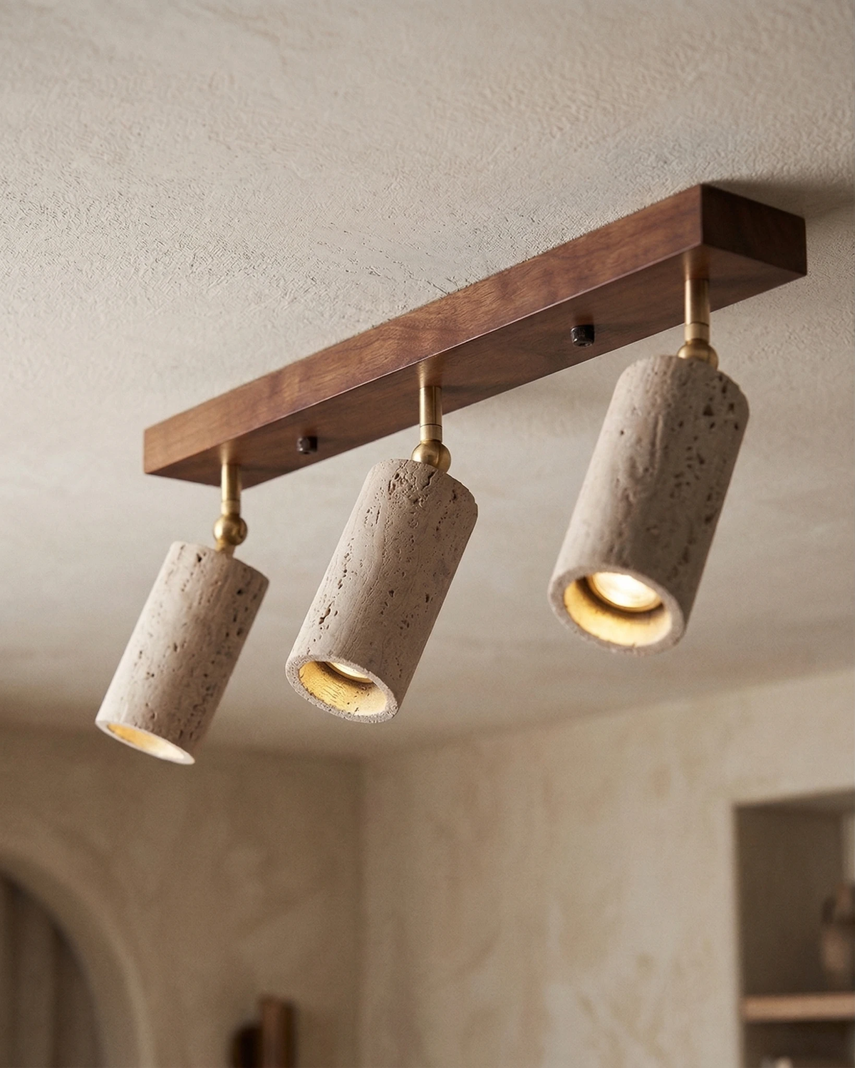Close-up of the travertine flush mount ceiling light PIETRA No.04, three spots lit on a walnut bar with brass pivots