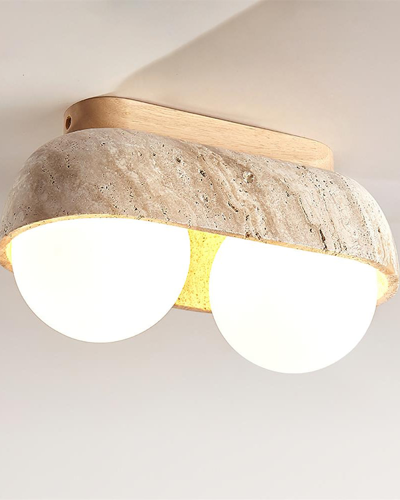 Close-up of the PIETRA No.03 travertine flush mount ceiling light, Two-Globe in Light Wood, both opal globes glowing