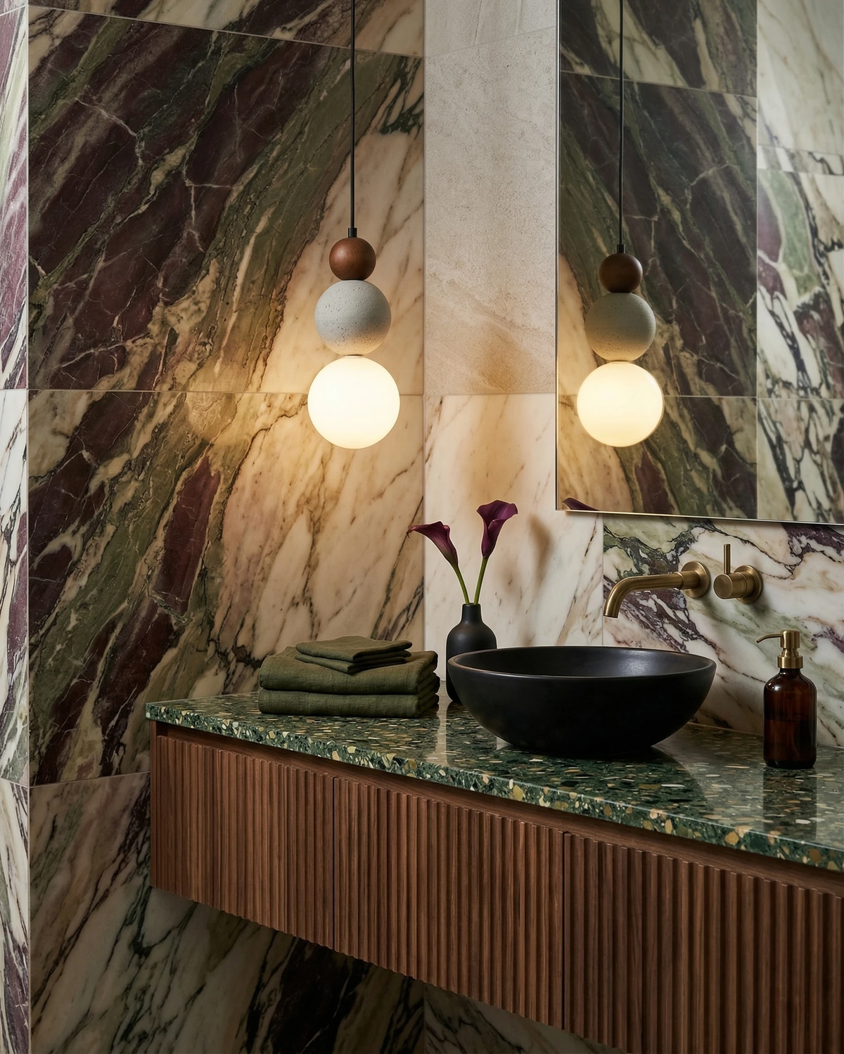Two travertine pendant lights DOMUS No.04 lit against a green and burgundy marble wall above a black basin