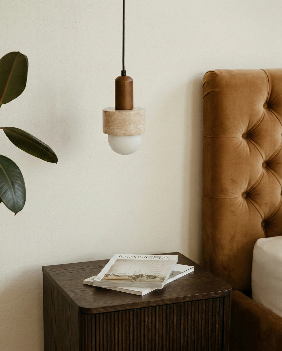 Travertine pendant light TONDO No.05 lit beside a tufted camel headboard above a fluted black nightstand