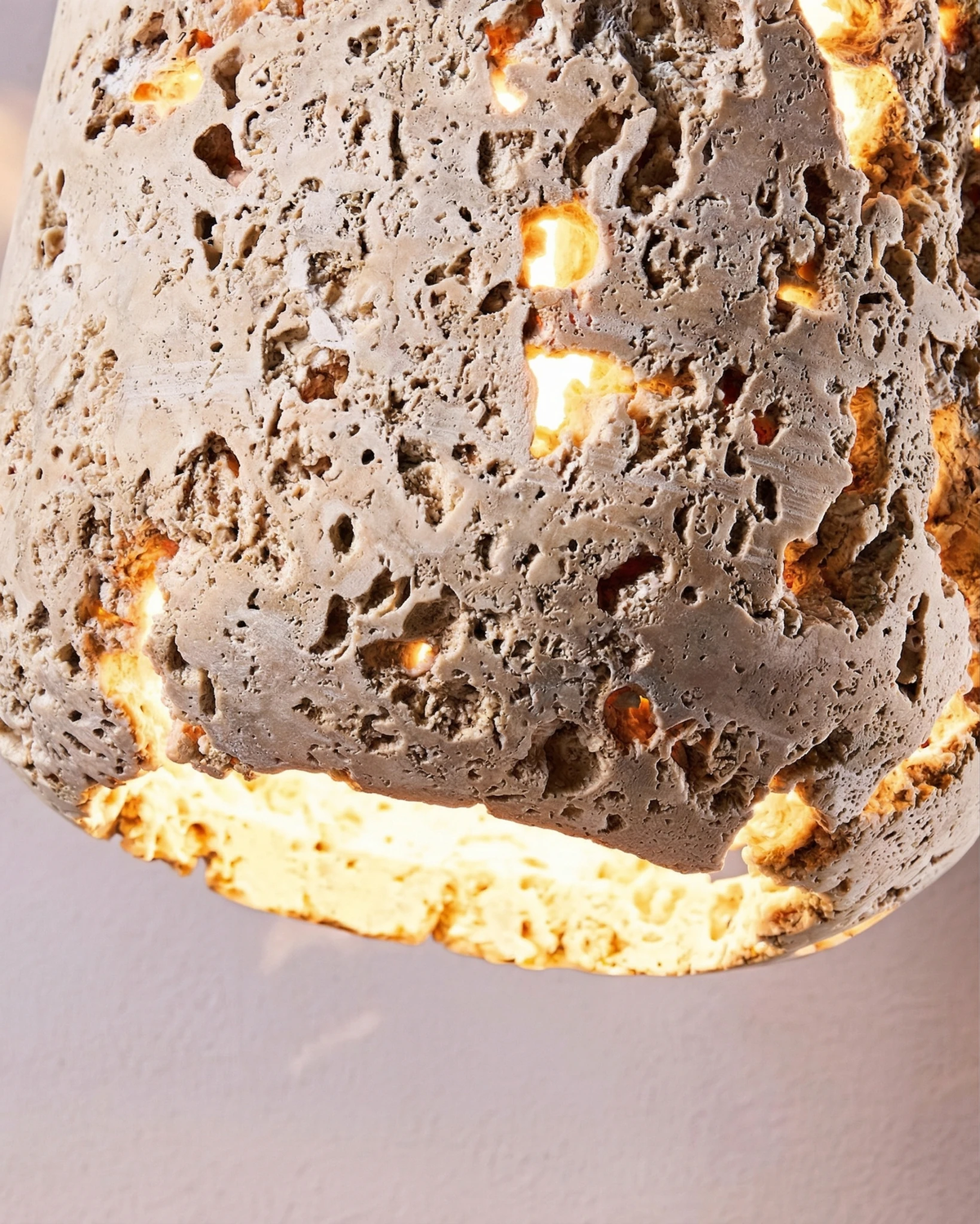 Close-up of the MASSA No.01 travertine pendant light, light glowing through the pores of the stone cylinder