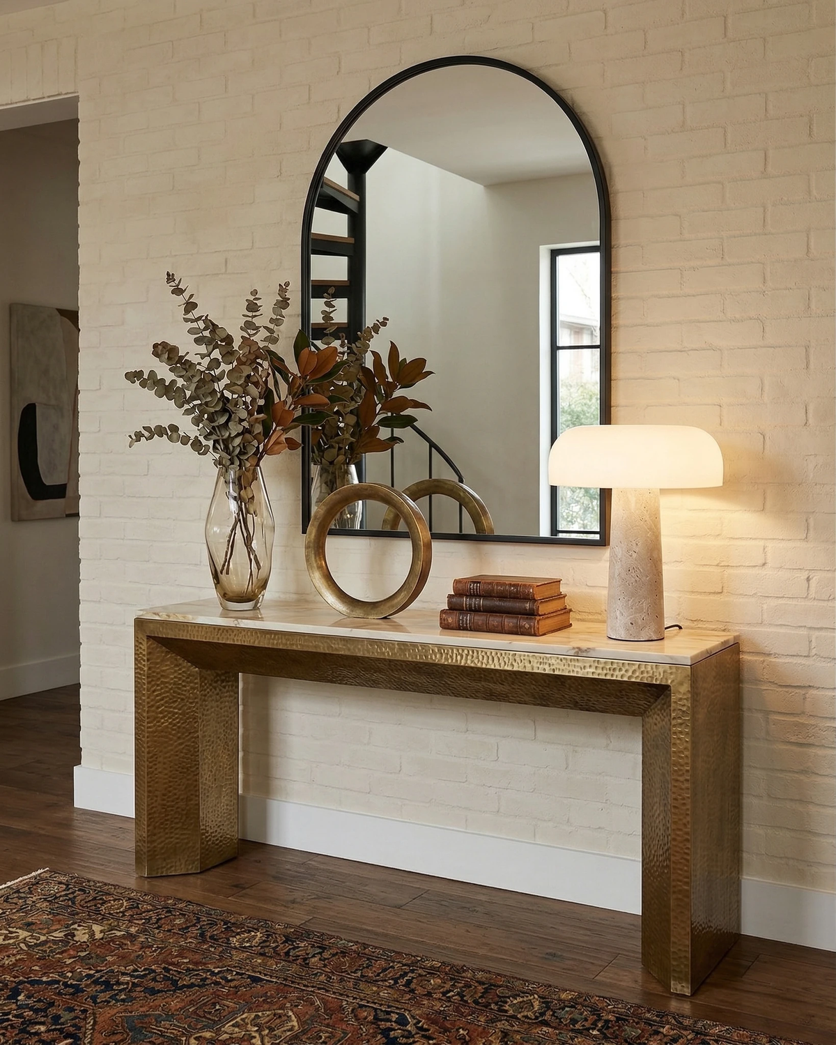 Travertine table lamp MORA No.03 switched on atop a wooden console below an arched mirror with dried flowers