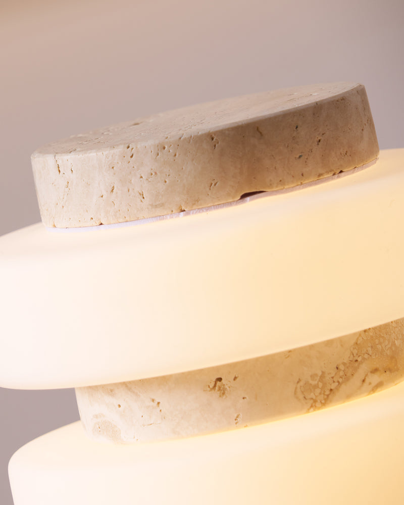 Close-up of the cream travertine tiers and glowing acrylic ring of the travertine table lamp PIETRA No.05