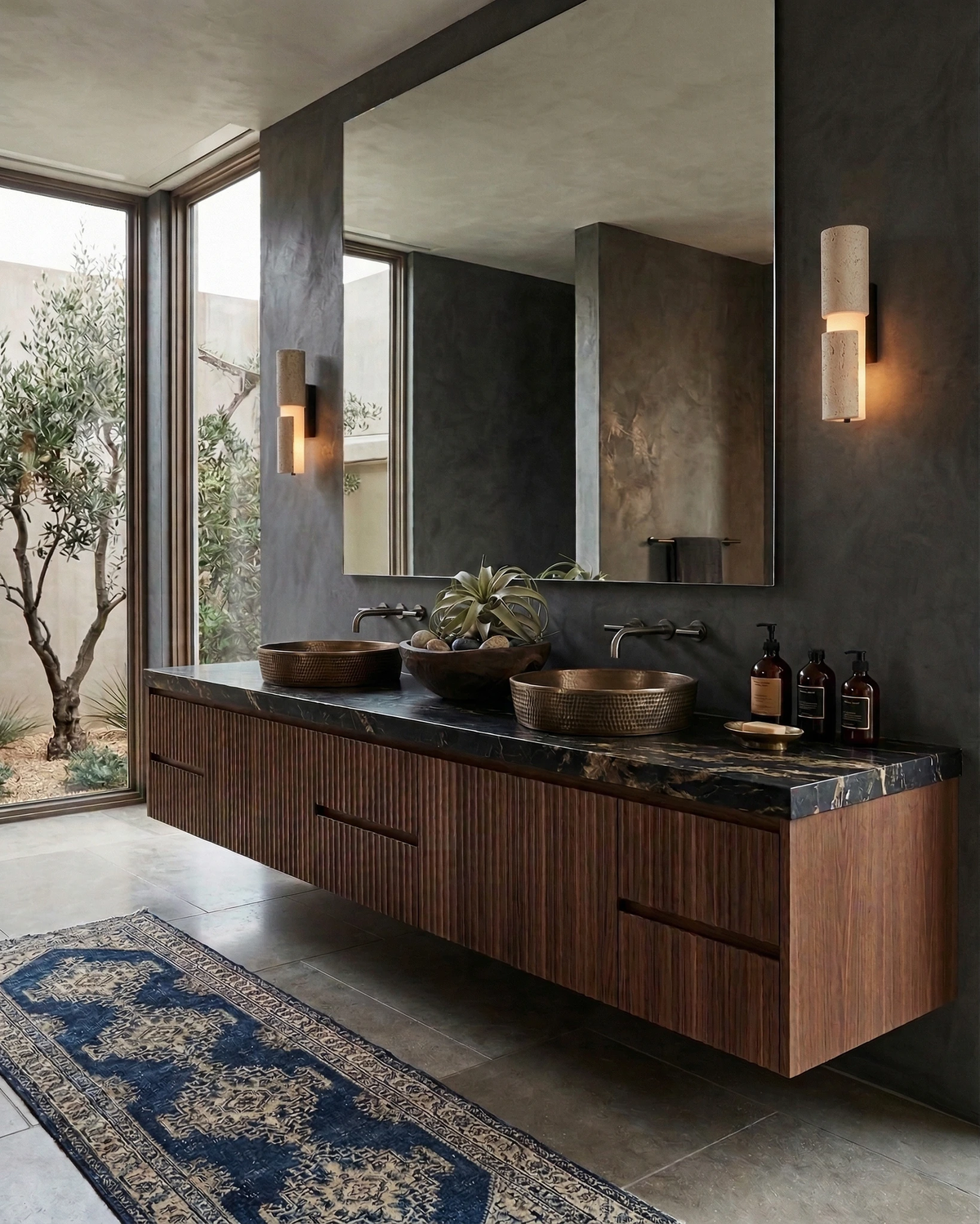Travertine vanity light NOTTI No.01 lit on a dark wall beside a mirror above a floating walnut double vanity