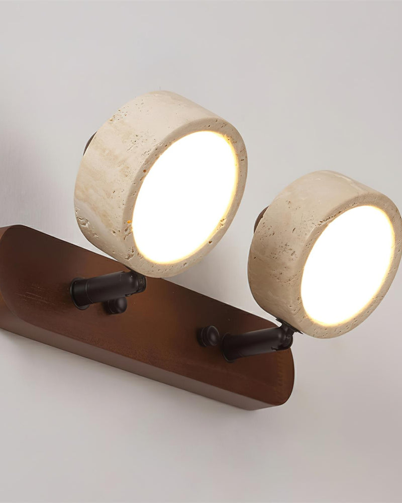 Close-up of two lit travertine drums on the dark walnut bar of the PIETRA No.02 travertine vanity light with pivot arms