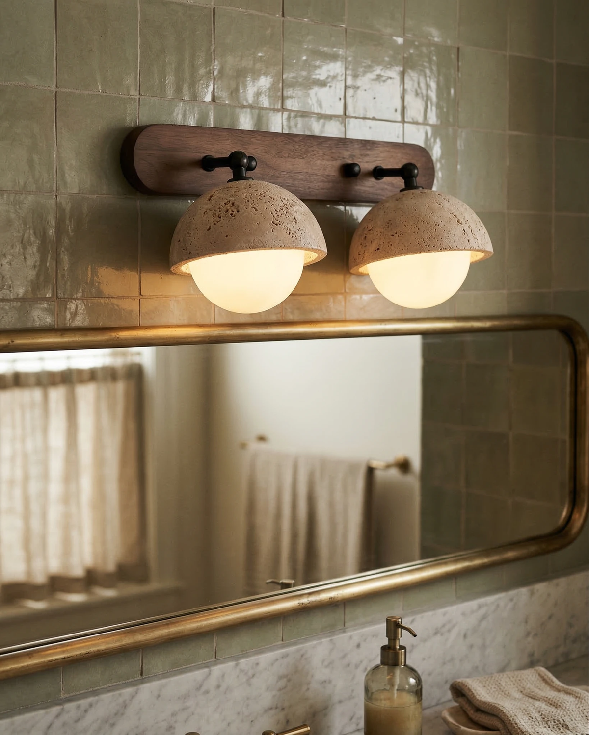 Travertine wall sconce AURA No.02 with two lit globes on green glazed tile above a brass-framed bathroom mirror