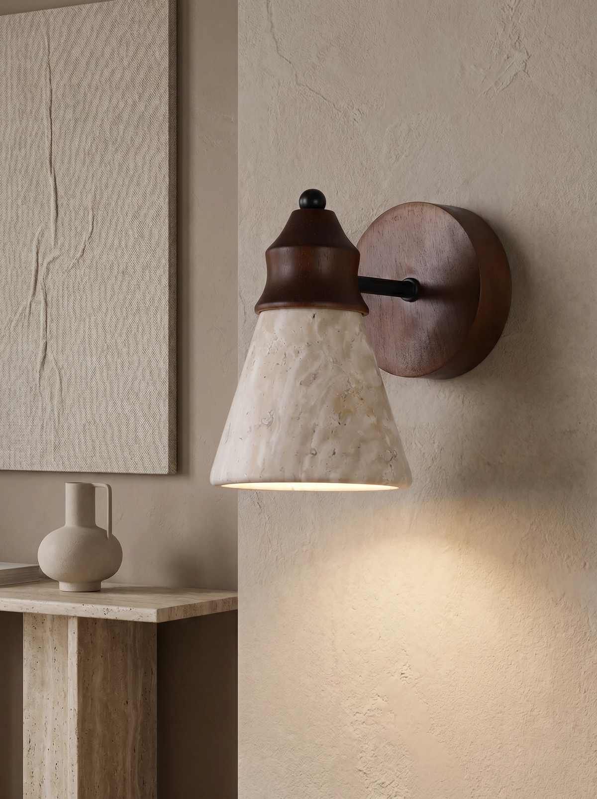 Travertine wall sconce CONA No.03 lit on a plaster wall above a travertine console with a small vase