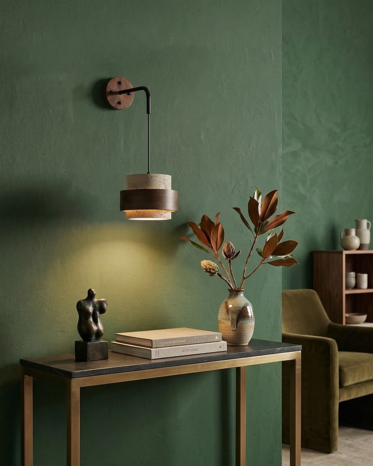 Travertine wall sconce TIVOLI No.02 switched on against a green wall above a wood console with a sculpture and books