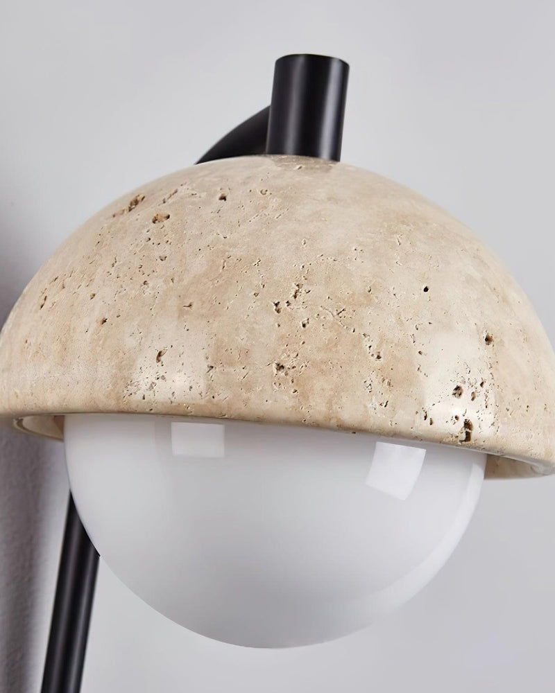 Close-up of the pitted yellow travertine dome and frosted glass globe of the AVORIO No.03 travertine wall sconce
