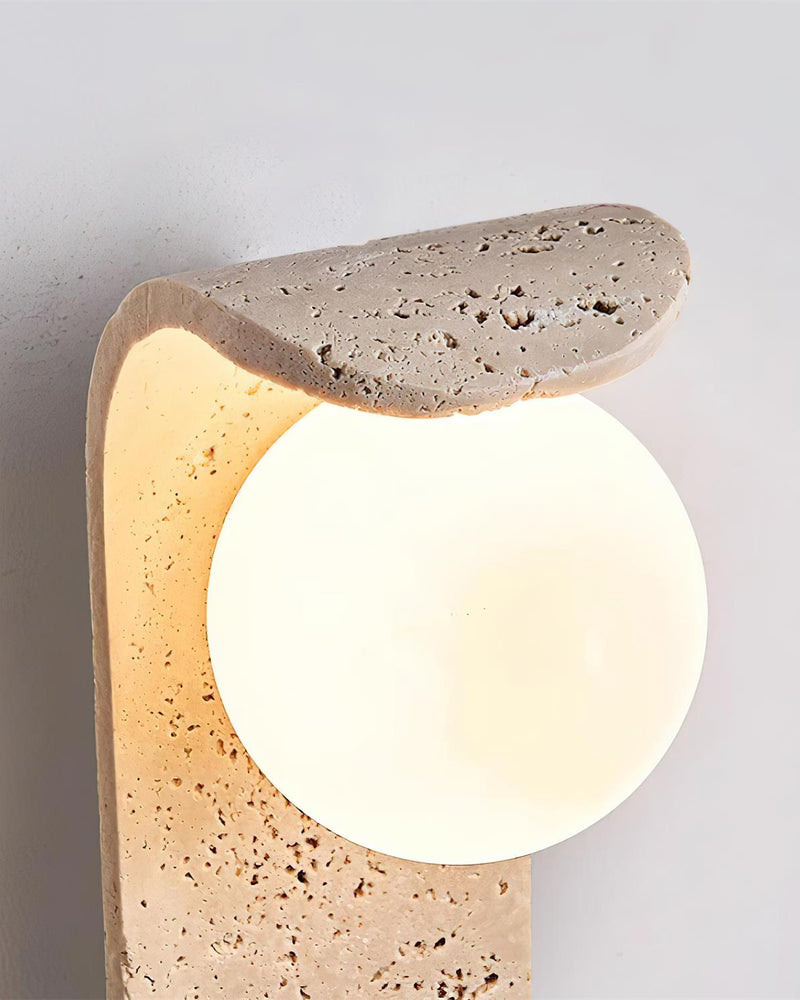 Close-up of the travertine wall sconce ARCO No.01 with the globe glowing under the pitted travertine curve