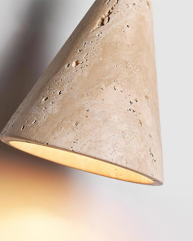 Close-up of the travertine cone shade of the CORTO No.01 wall sconce lit from within, pitted cream stone surface