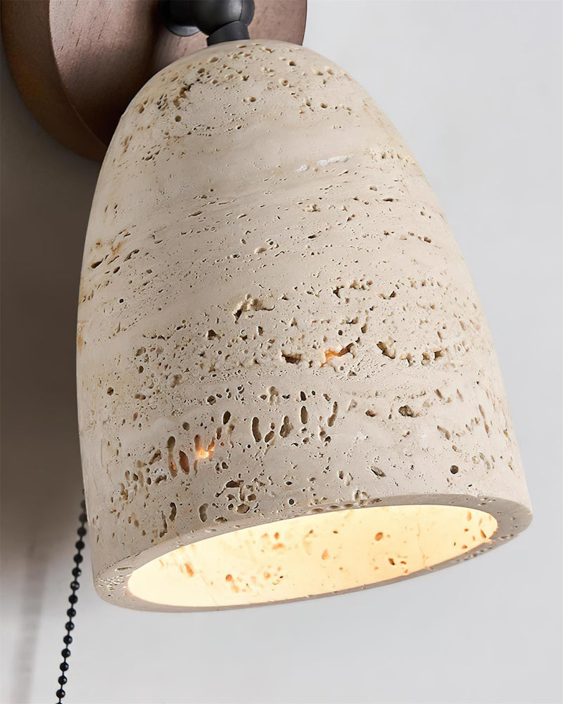 Close-up of the pitted travertine dome and pull chain of the travertine wall sconce PERA No.01, lit inside