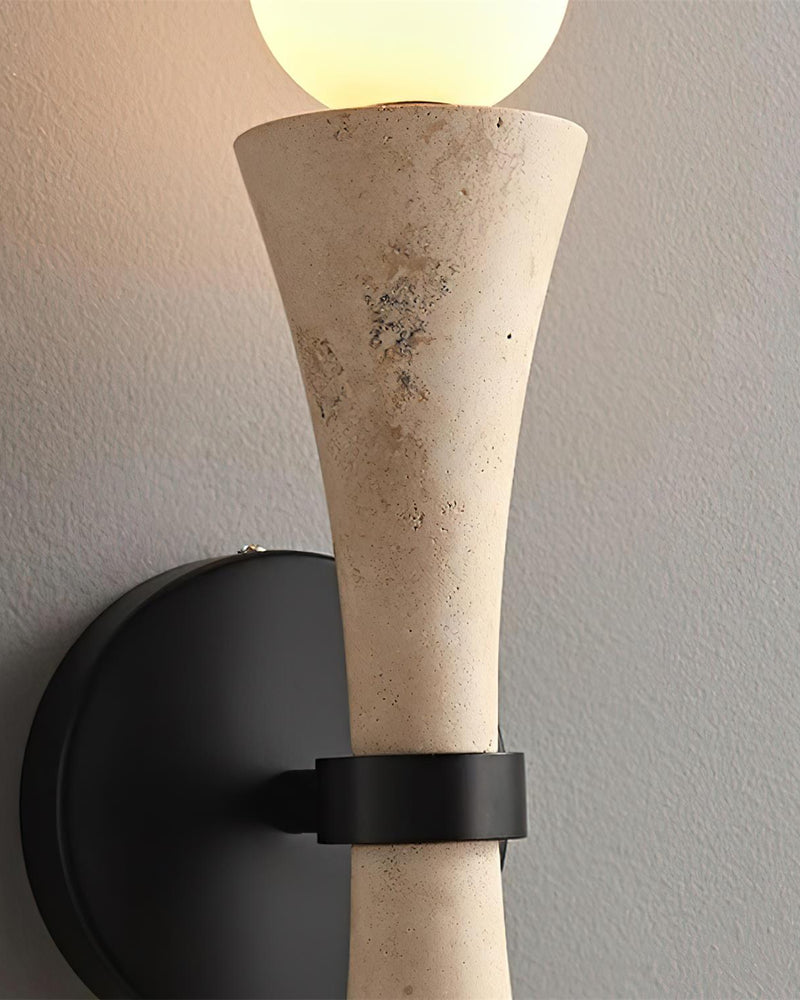 Close-up of the travertine wall sconce VETTA No.01 showing the black bracket and the lit upper globe