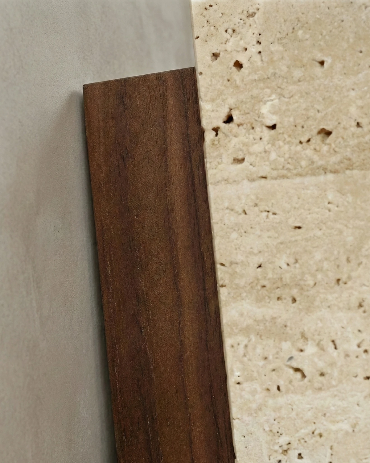 Close-up of the GRANO No.01 travertine wall sconce, pored yellow travertine beside a dark walnut edge