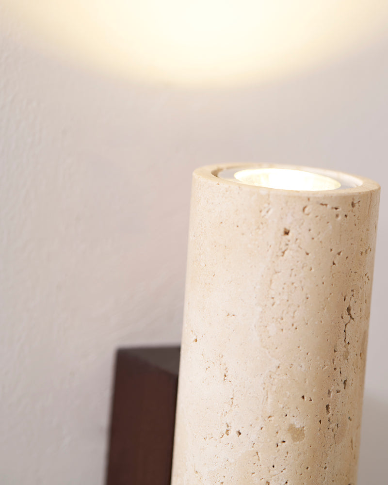 Close-up of the top of the travertine wall sconce STELO No.02 switched on, washing light up the wall
