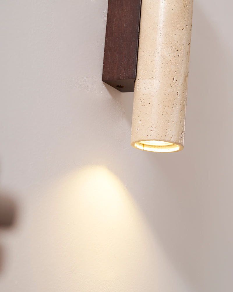 Close-up of the lit travertine wall sconce STELO No.02 casting a pool of light down the wall below