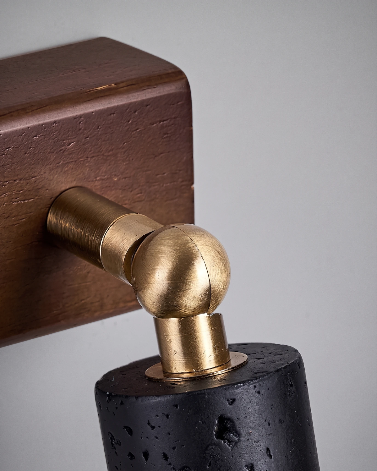 Close-up of the brass ball joint linking the walnut block and black stone head of the VITRU No.01 travertine wall sconce