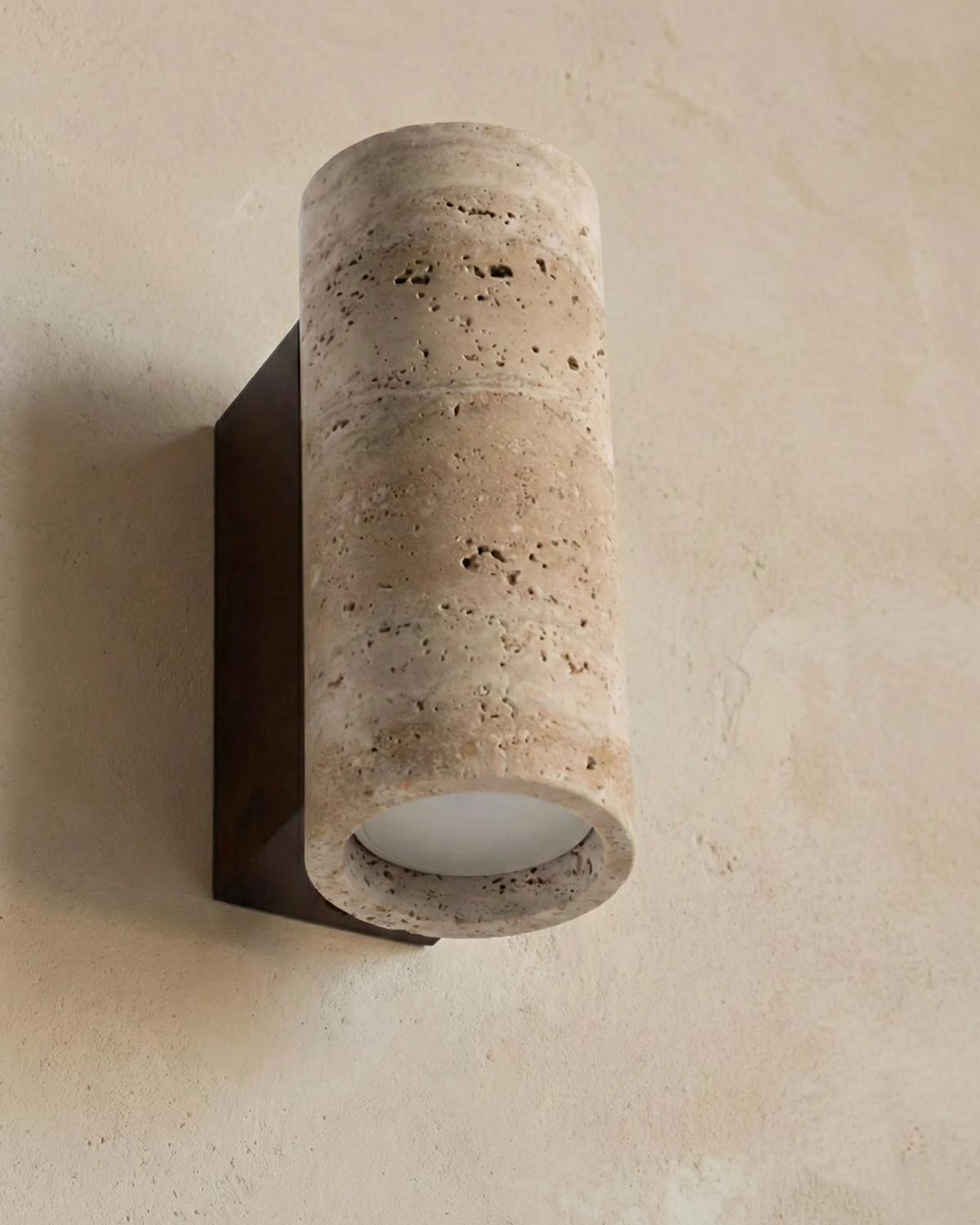 Close-up from below of the travertine wall sconce GRANO No.02 cylinder showing the downlight lens
