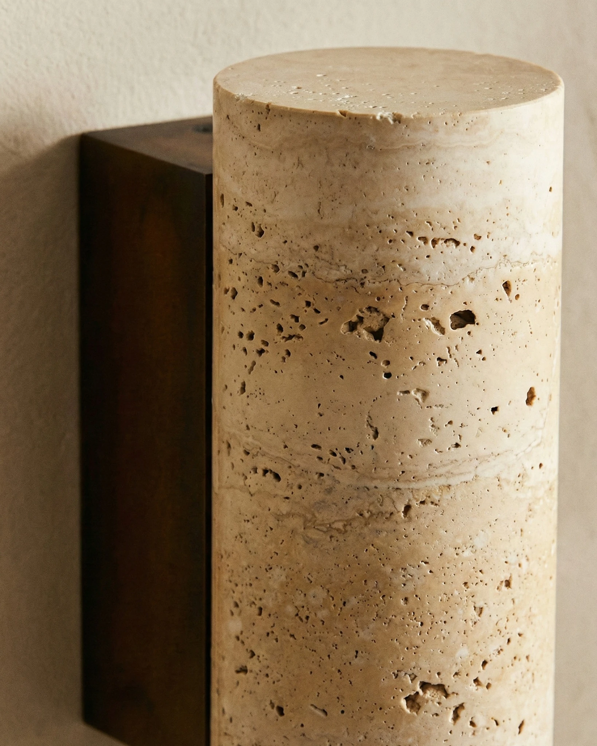 Close-up of the porous yellow travertine and dark bracket of the travertine wall sconce GRANO No.02