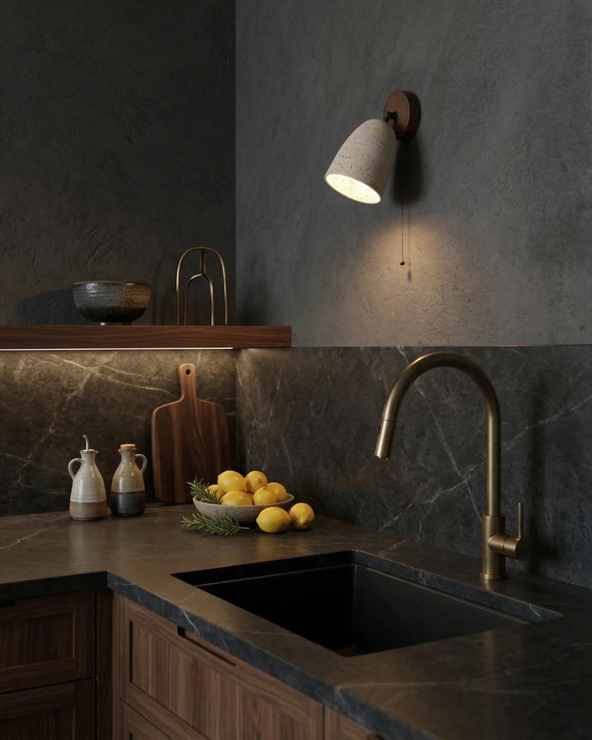 Travertine wall sconce PERA No.01 lit above a dark stone kitchen counter with a brass faucet and lemons