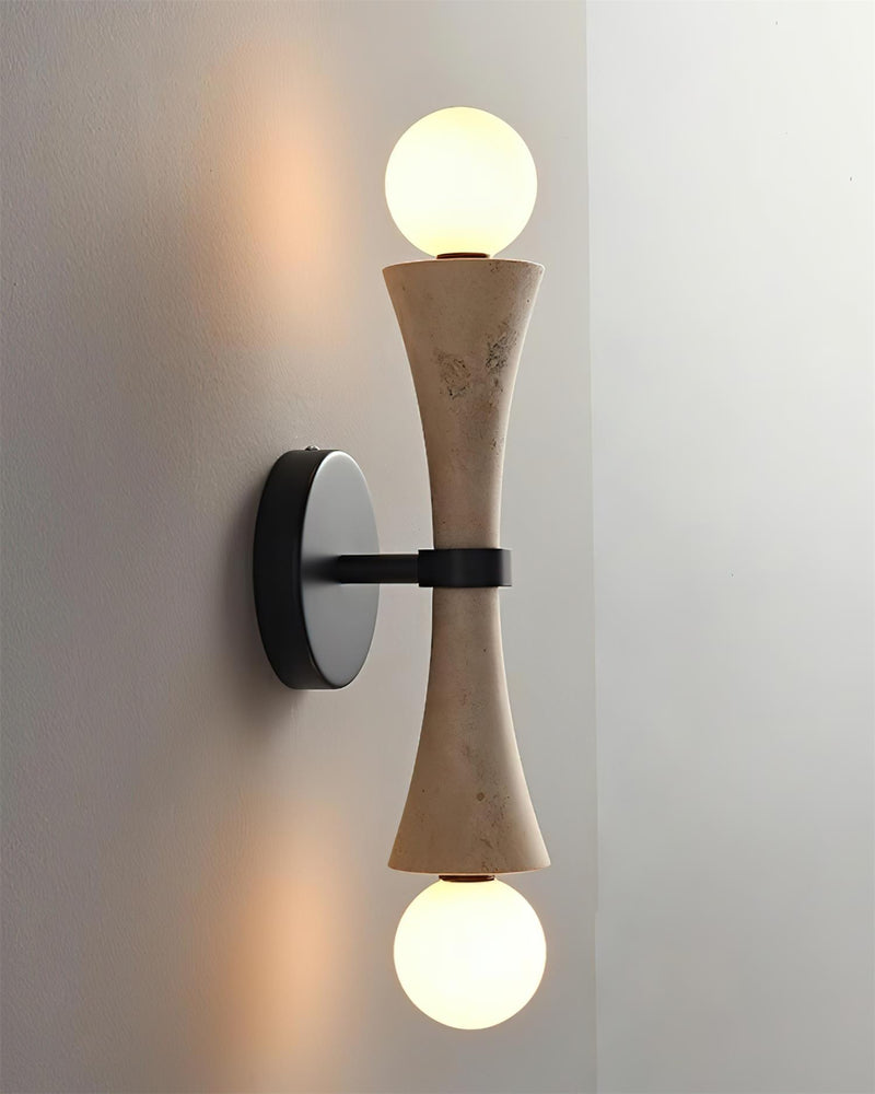 Travertine wall sconce VETTA No.01 lit, angled view of the hourglass stone with warm light washing the wall