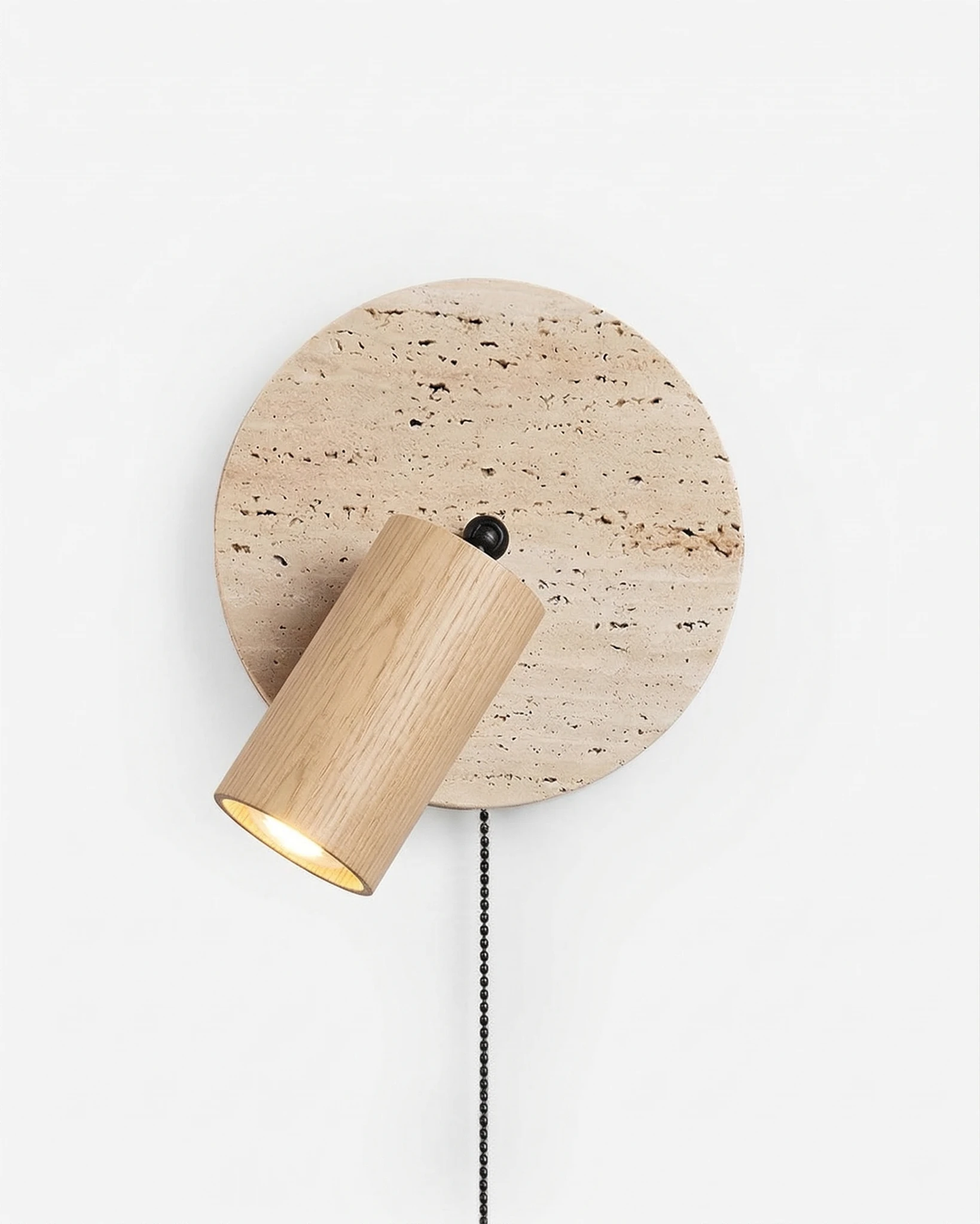 Travertine wall sconce VITRU No.03 in Light Oak, pale wood spotlight glowing against a travertine disc with pull chain