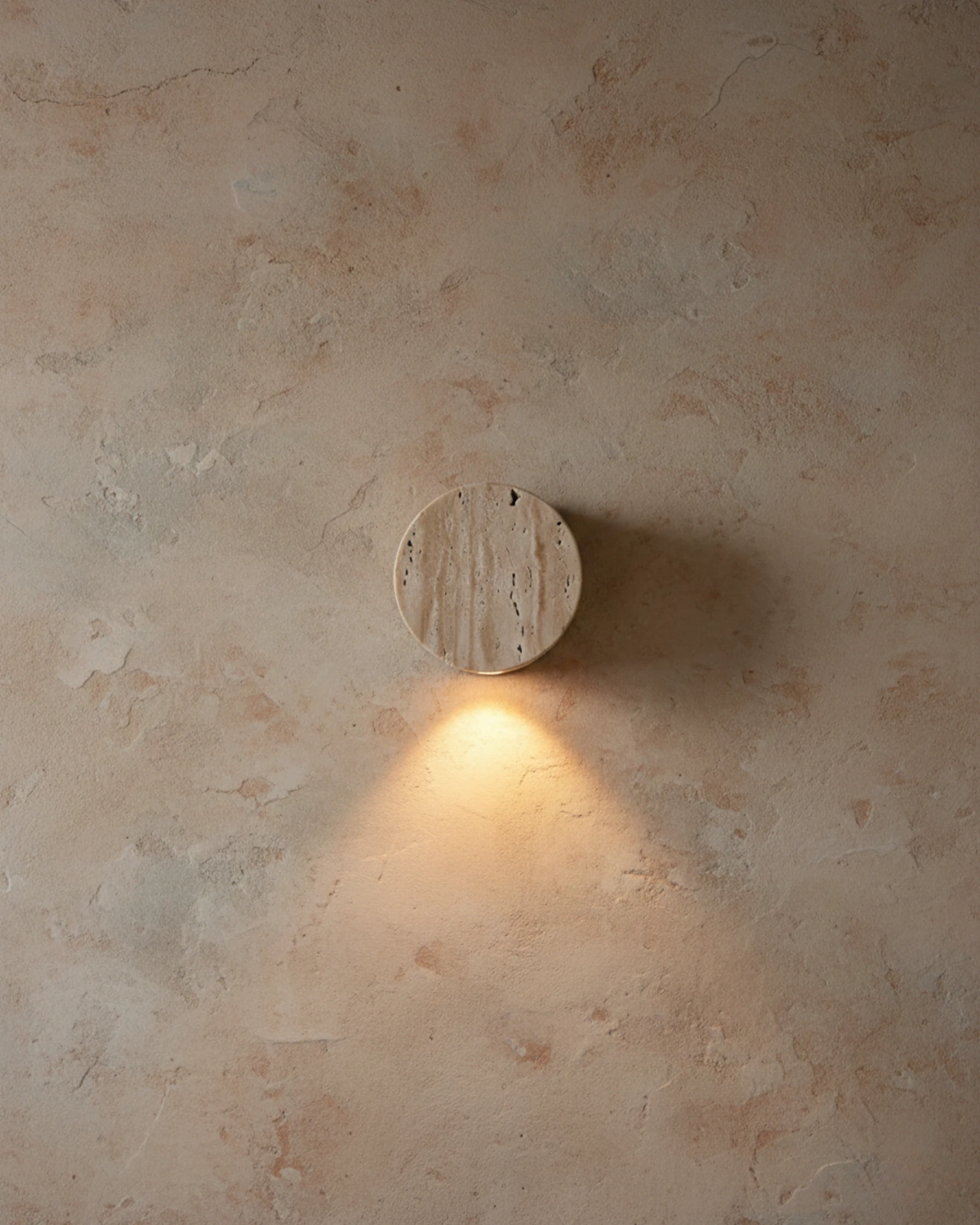 Travertine wall sconce VERONA No.01 on a pink-toned plaster wall, round travertine disc lit from beneath