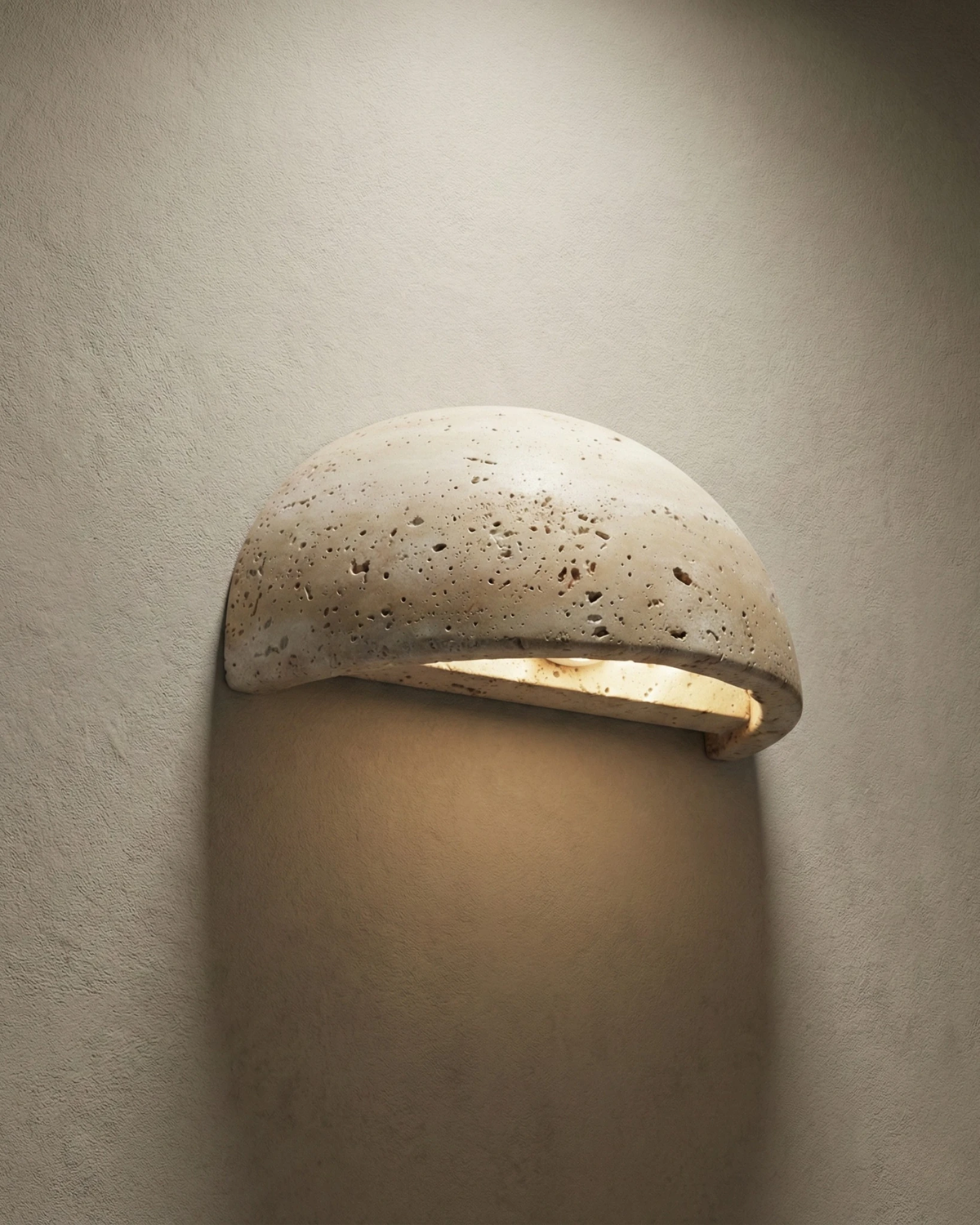 Travertine wall sconce BERGAMO No.01 half-moon downlight switched on, warm light washing a beige plaster wall