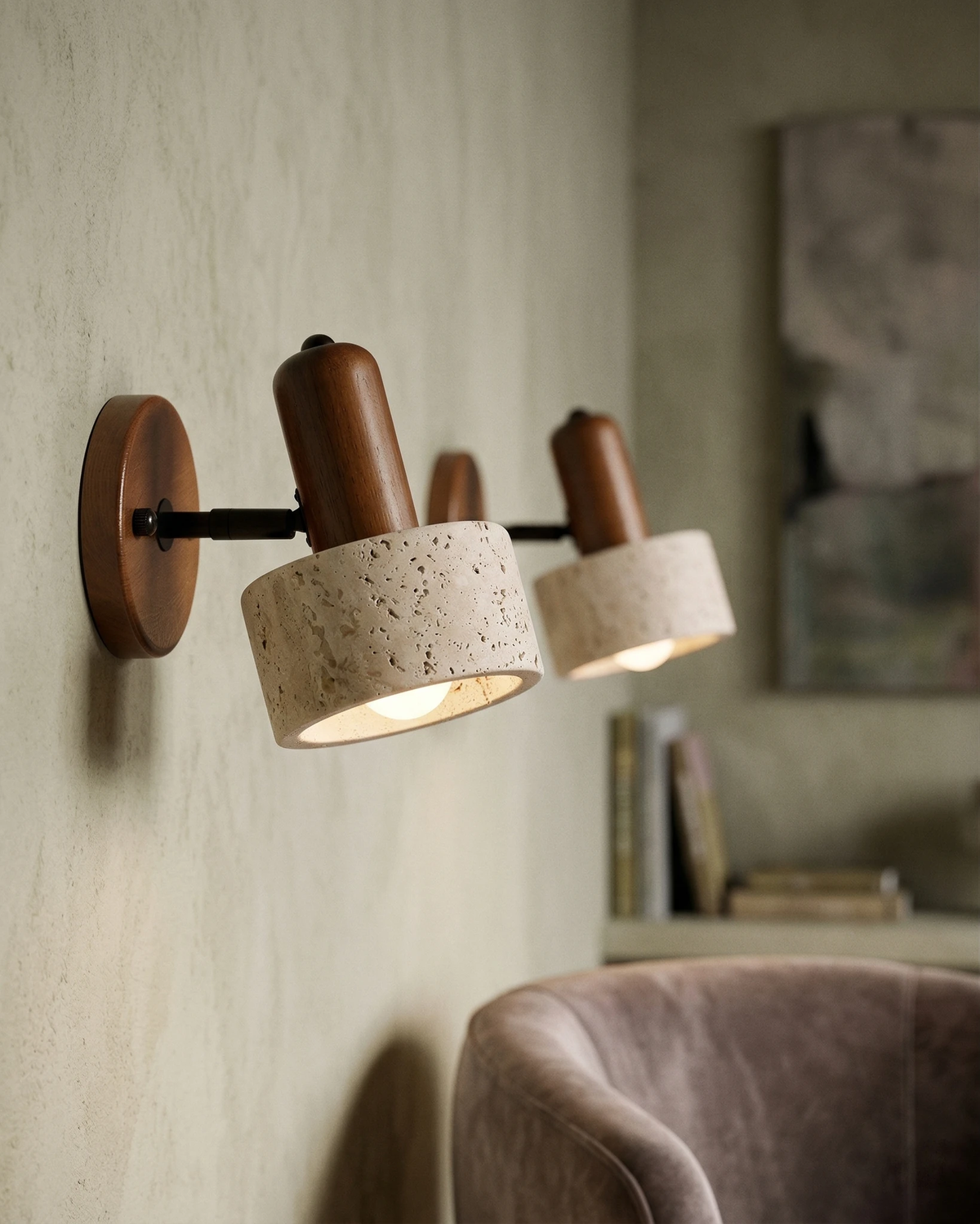 Travertine wall sconce CONA No.01, cylinder head on dark walnut pivoted and lit beside a velvet armchair