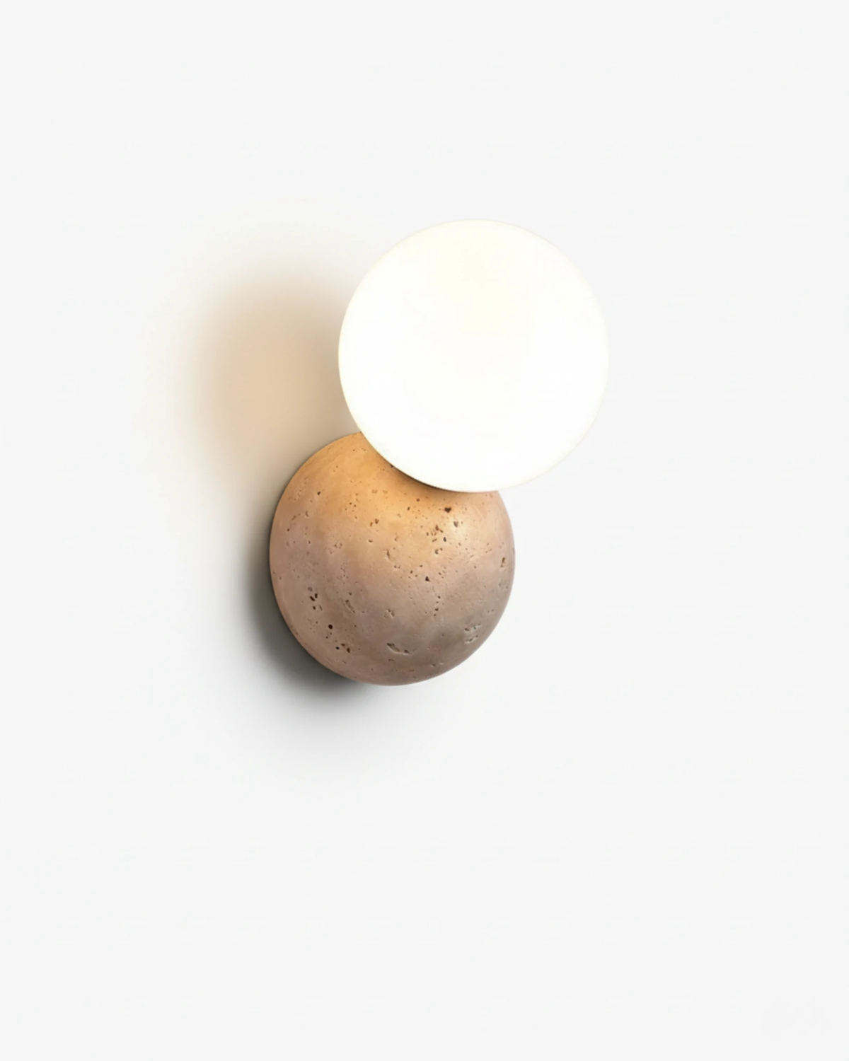 Travertine wall sconce MARE No.01, textured travertine disc with a white glass globe, unlit on a white wall