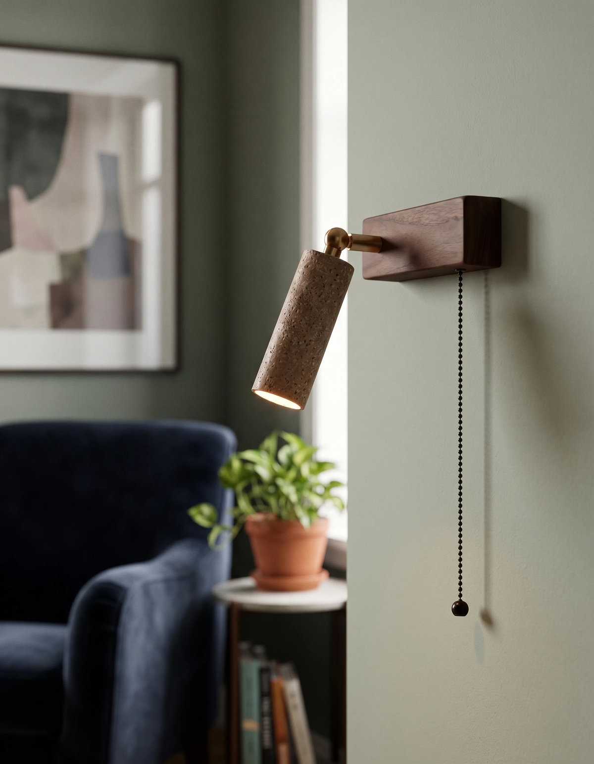Travertine wall sconce VITRU No.01, cream travertine head lit above a navy armchair with a potted plant