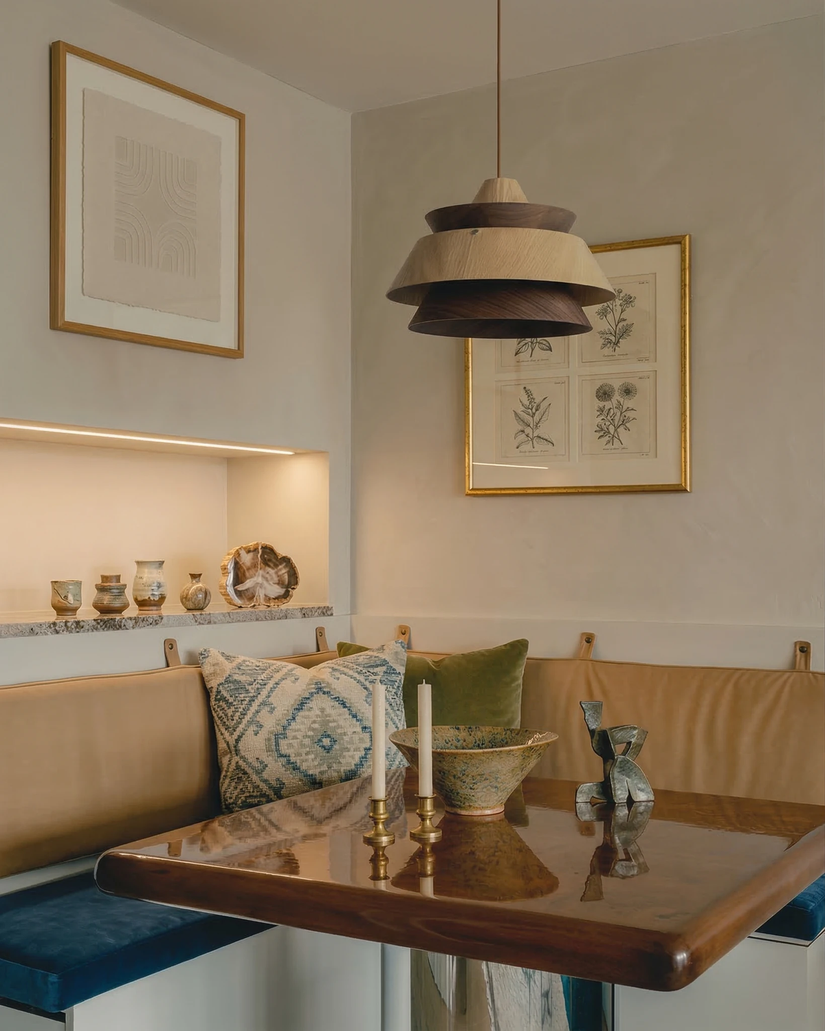 Wood pendant light BOSCO No.01 lit above a banquette dining nook with a wooden table and botanical prints