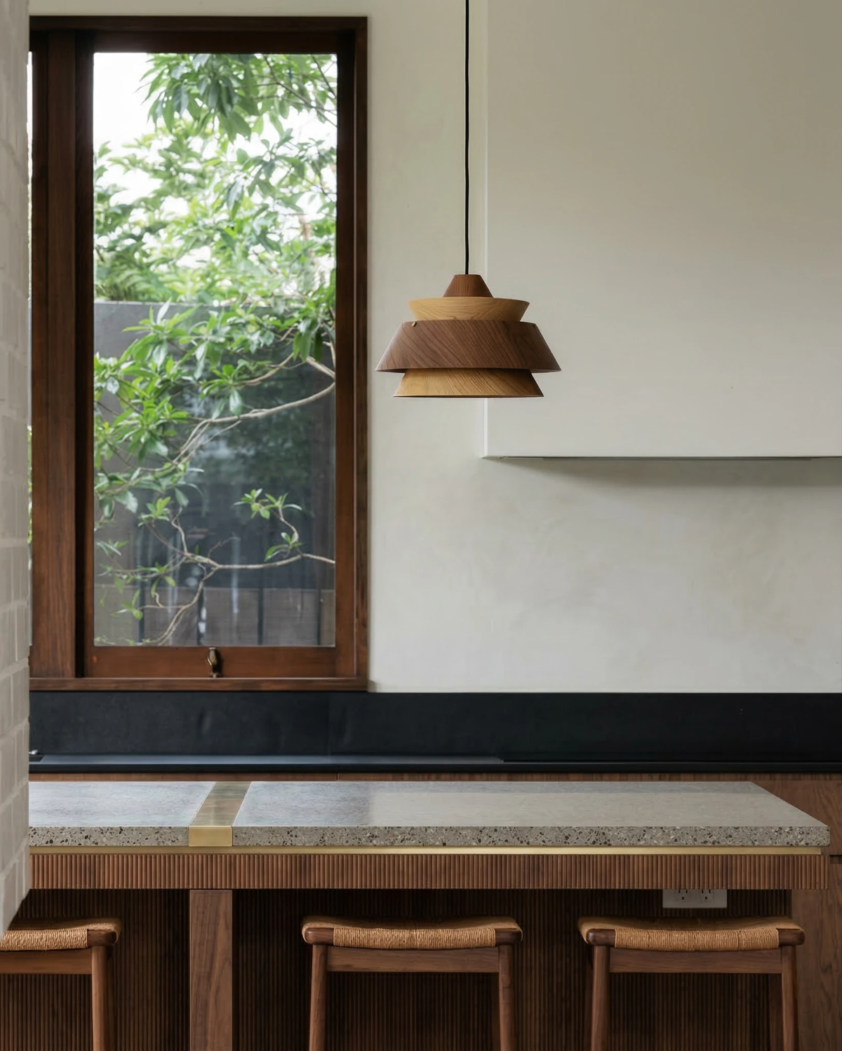 Wood pendant light BOSCO No.01 hanging over a stone kitchen counter with wooden bar stools beside a garden window