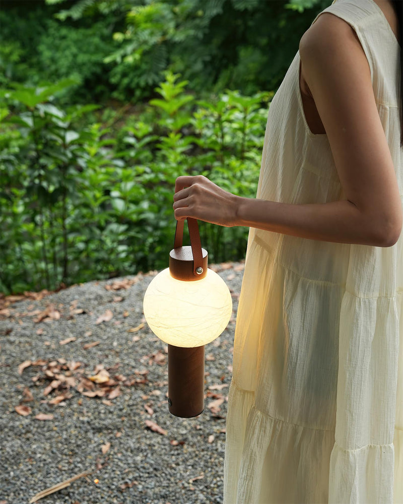 Wood table lamp NAPOLI No.01 held by a woman in a white dress among green foliage, lantern lit
