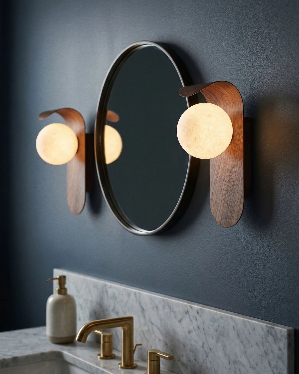 Two wood wall sconces RIMINI No.01 in walnut lit either side of a round mirror above a marble vanity with brass taps