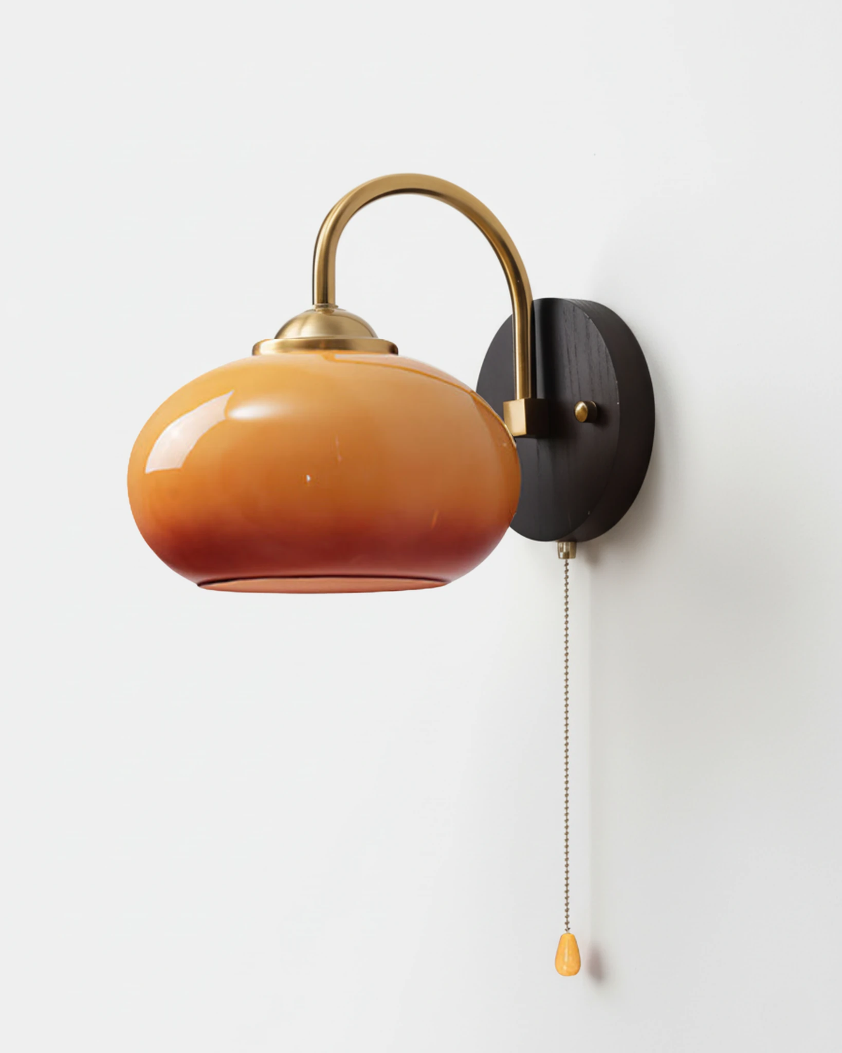 Wood wall sconce CURVA No.02 in Caramel, amber-to-red glass shade on an arched brass arm with a brass pull chain