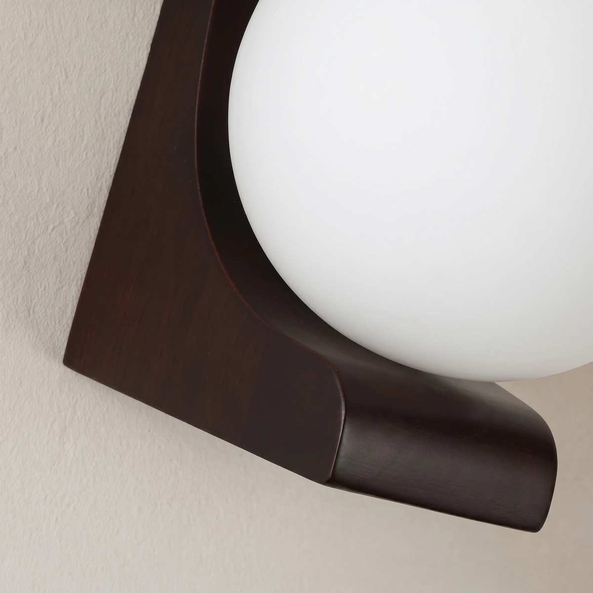 Close-up of the curved dark walnut bracket cradling the frosted glass globe of the CURVA No.01 wood wall sconce