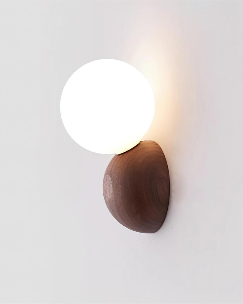 Wood wall sconce ALBE No.01 from the side, lit opal globe perched on the rounded walnut pebble mount